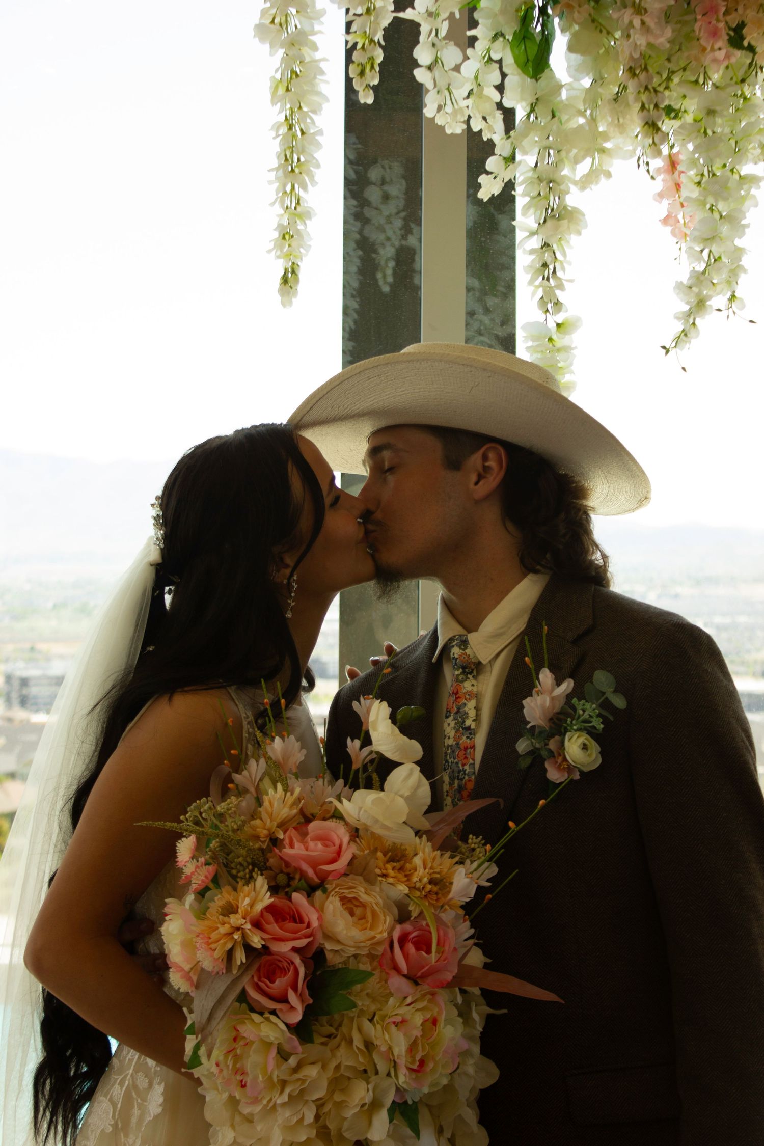 A bride and groom share a kiss at the altar, with floral decorations above.