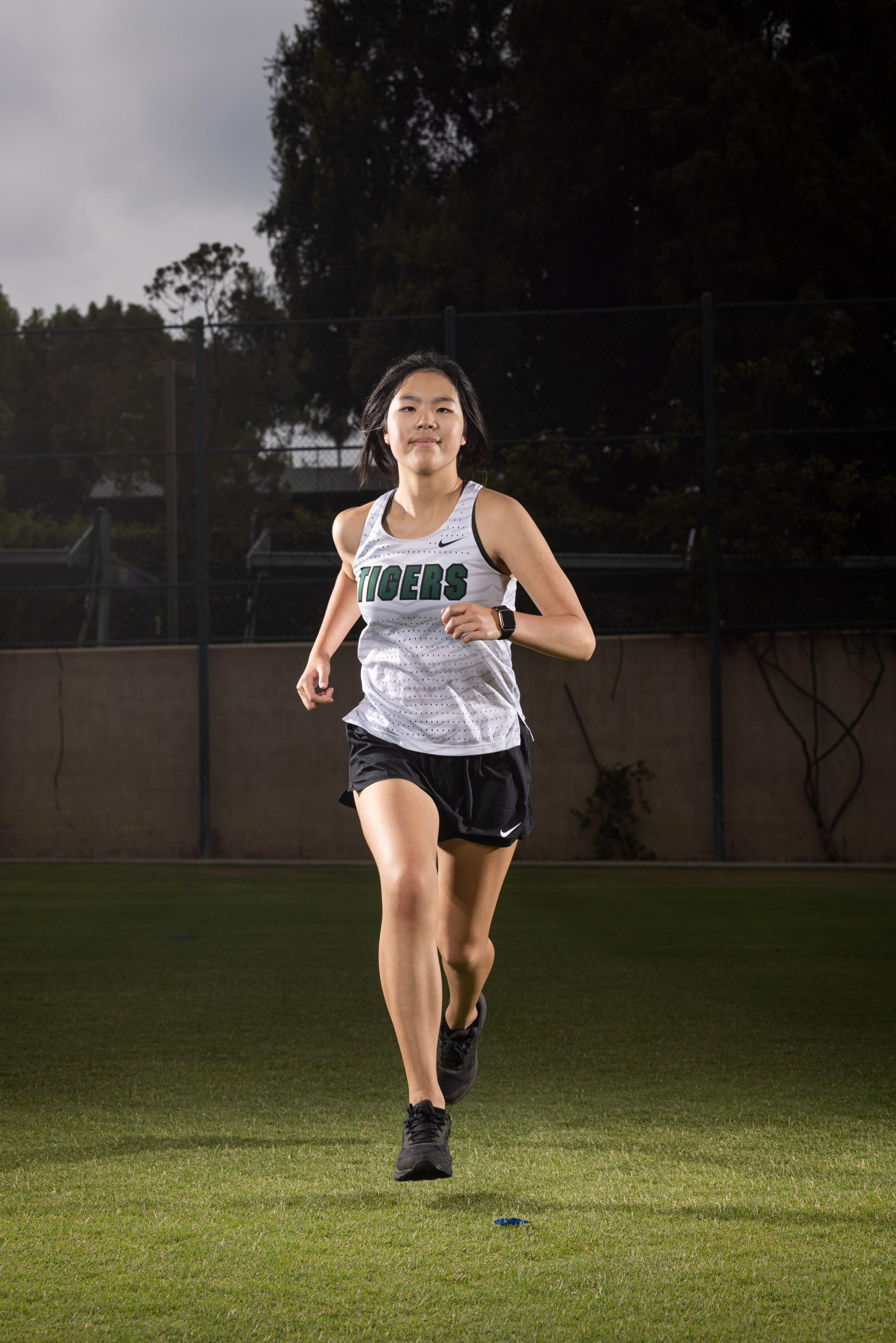 Athletic runner sprinting across a dark grass field at night under dramatic lighting.