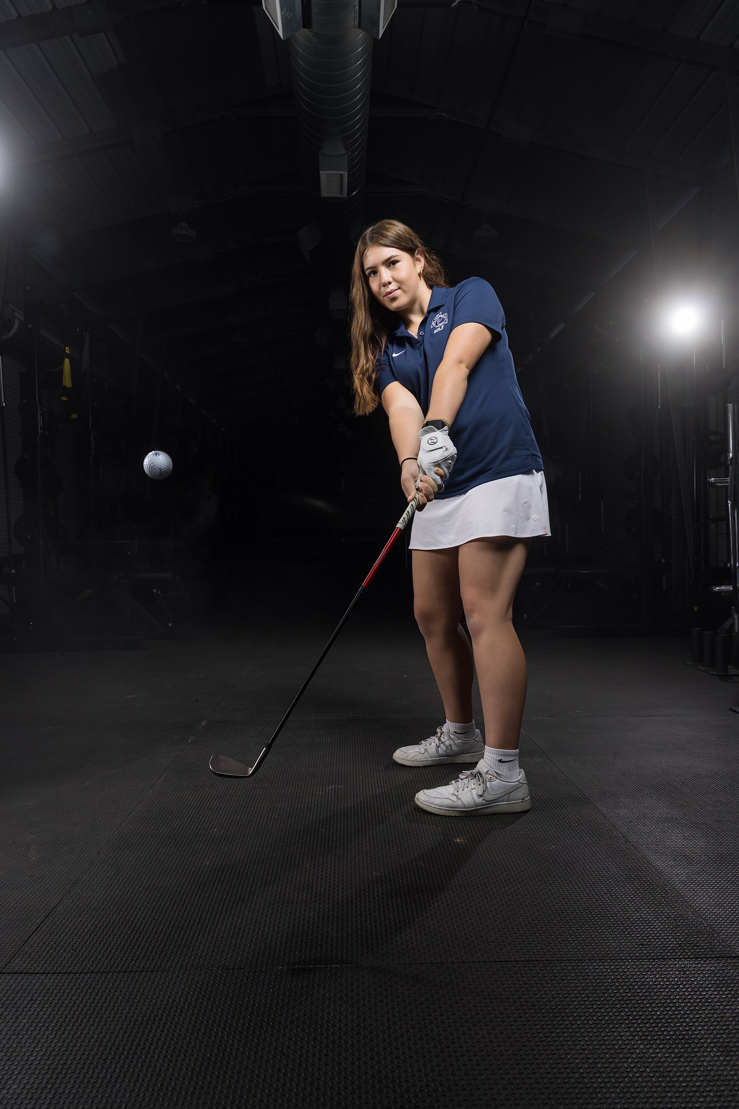 A golfer in a navy shirt and white shorts practices their putting stance on a dark indoor green.