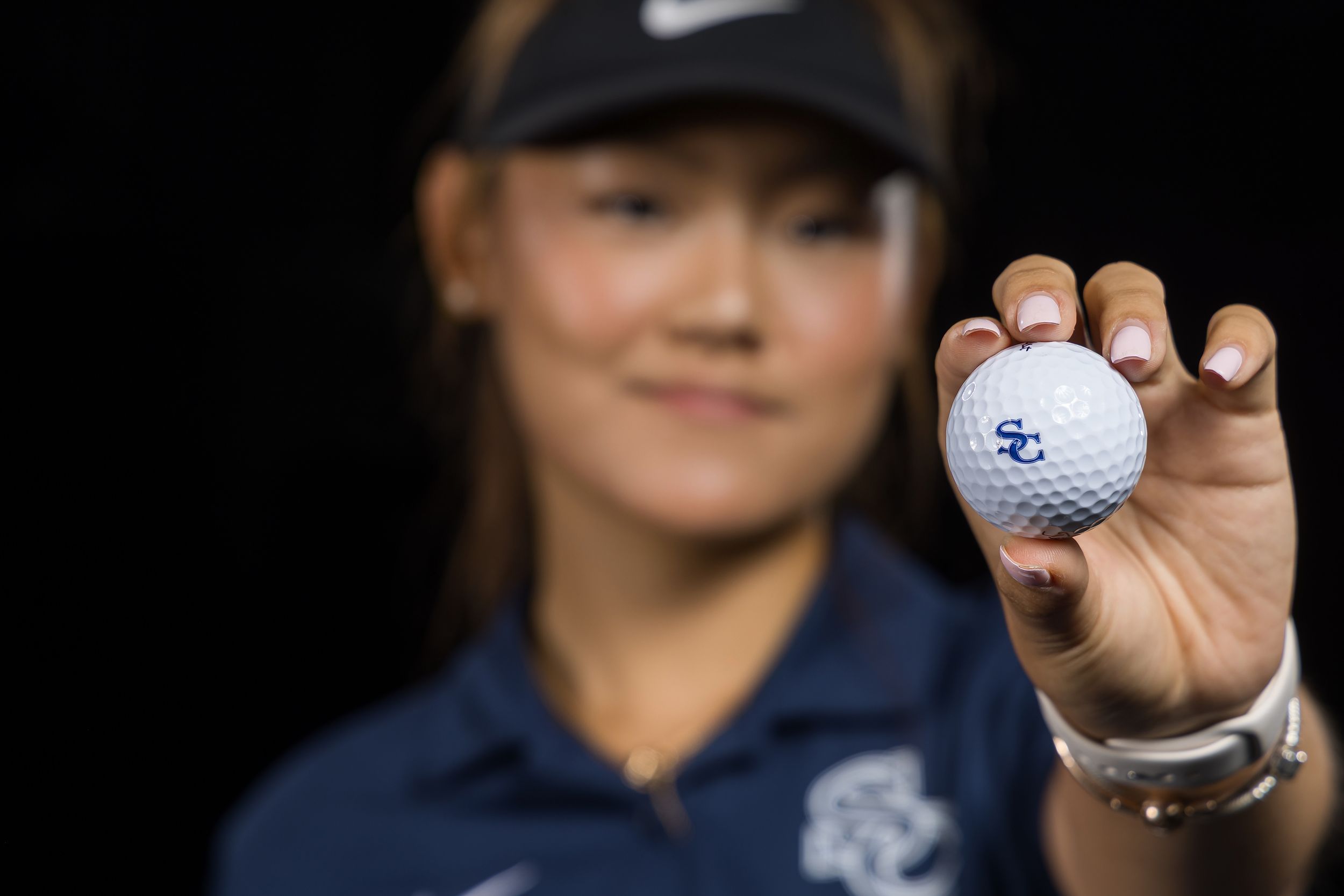 A golf ball is held up close to the camera against a dark background, showing details of its dimpled surface.