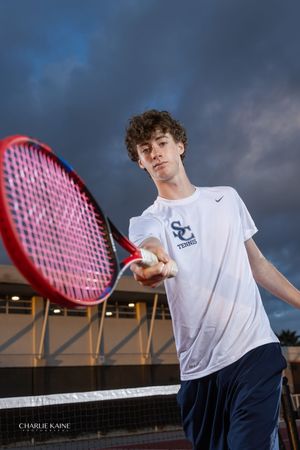 Student athlete practices tennis serves on court at dusk wearing Serra Canyon uniform.