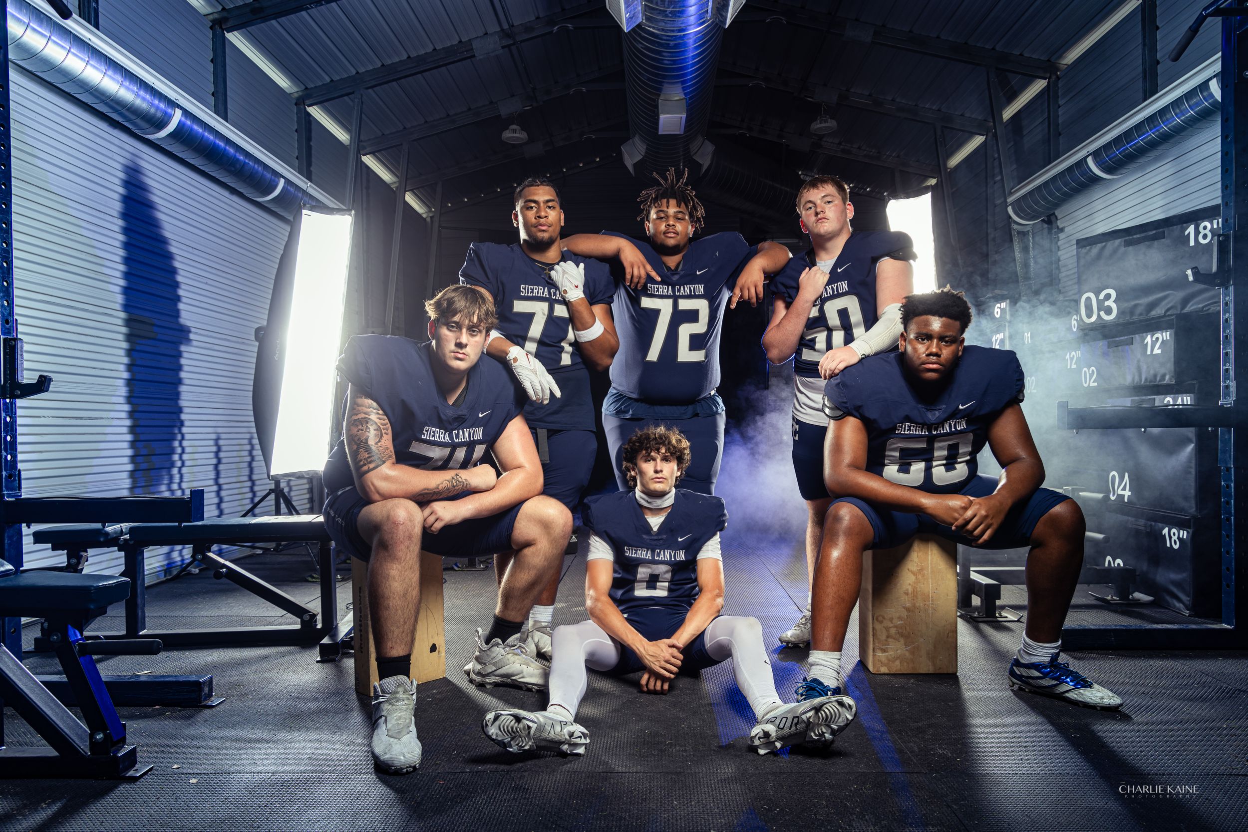 Football players in navy uniforms pose together in weight room for team photo.