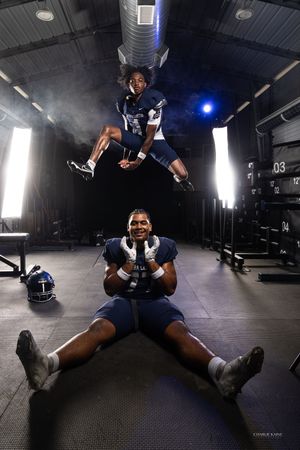 Athletic photoshoot with one player jumping while another sits on gym floor.