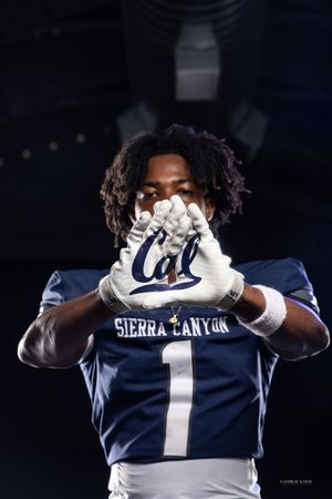 Football player in navy Sierra Canyon jersey holding up gloves showing team logo.