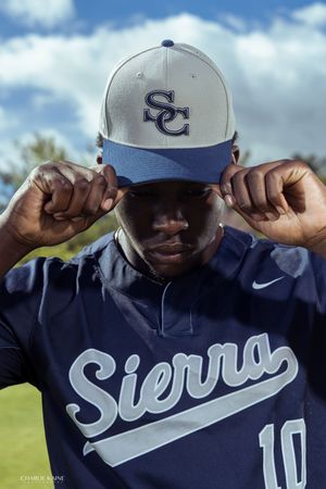 Baseball player adjusts Sierra College cap while wearing navy uniform with number 10.