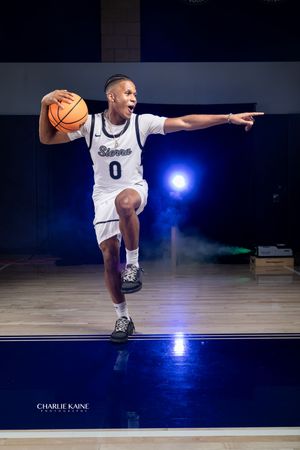 Basketball player in white uniform dribbling on court with dramatic lighting.