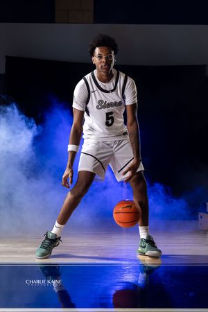 Basketball player in white Sierra Canyon uniform dribbling against blue smoke background.