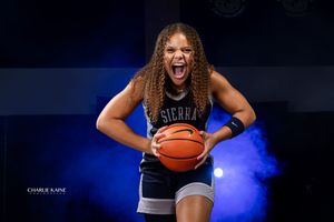 Basketball player shows energetic expression while holding ball against dark background with blue lighting.