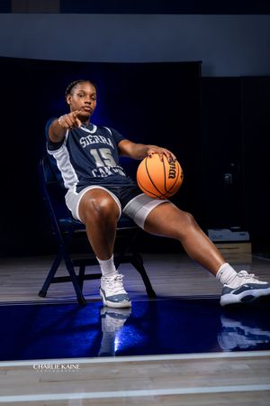 Basketball player poses seated in chair with dramatic lighting on court while holding ball.