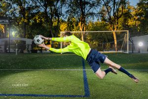 Soccer goalkeeper in neon yellow uniform makes diving save during sunset practice.