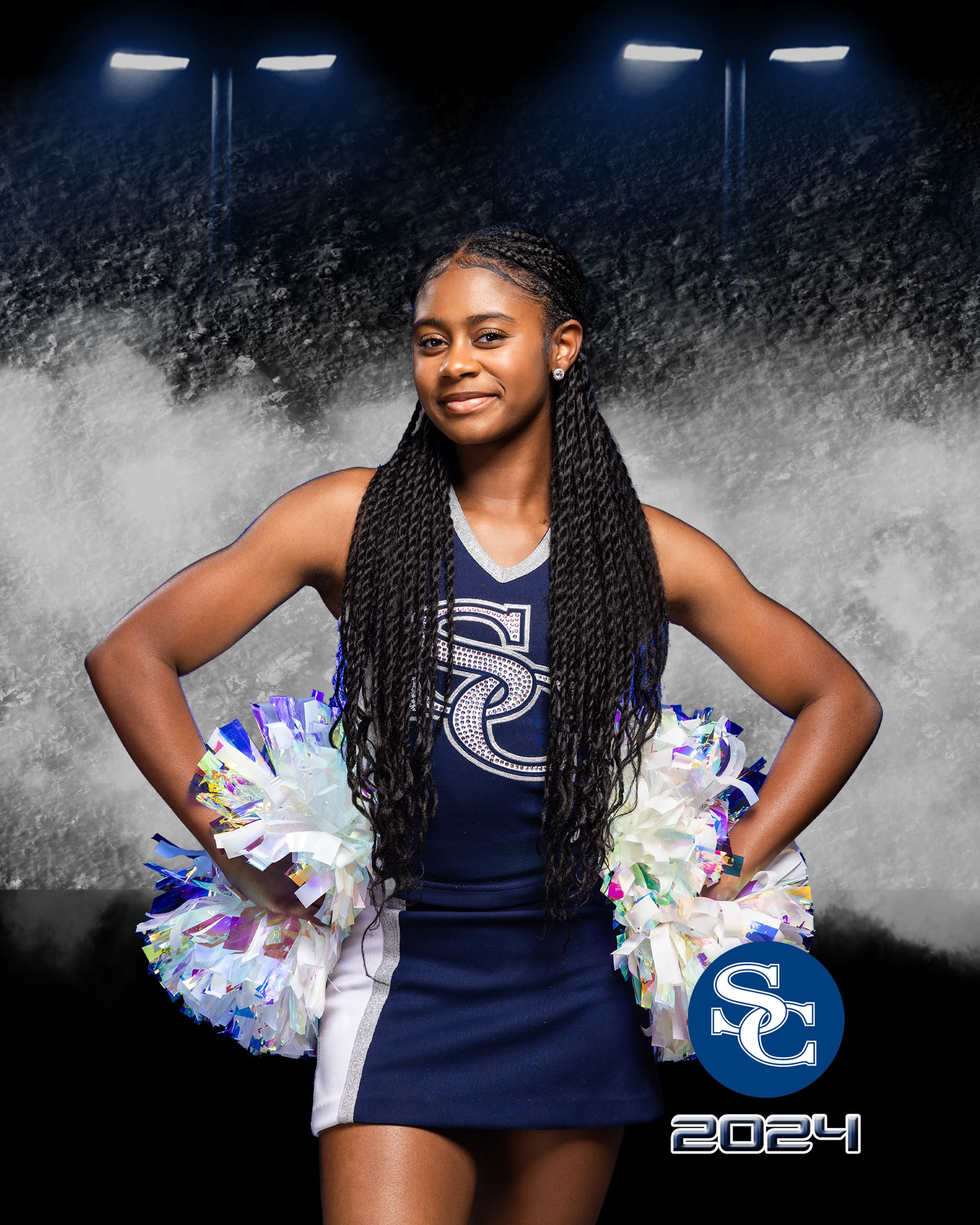 Cheerleader poses with pom poms in navy uniform against smoky background with stadium lighting.