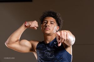 Athlete in navy tank top poses with raised fists against dark background.