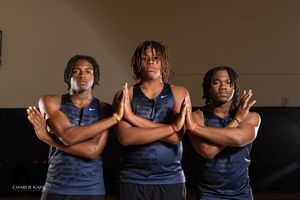 Three athletes in navy uniforms pose with crossed arms against dark background.