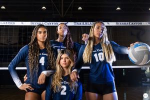 Volleyball team poses with balls in dramatic dark lighting for team photo.