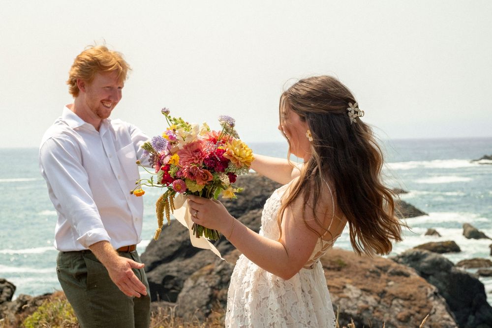 A couple sharing a joyful moment on a cliff overlooking the Pacific Ocean.