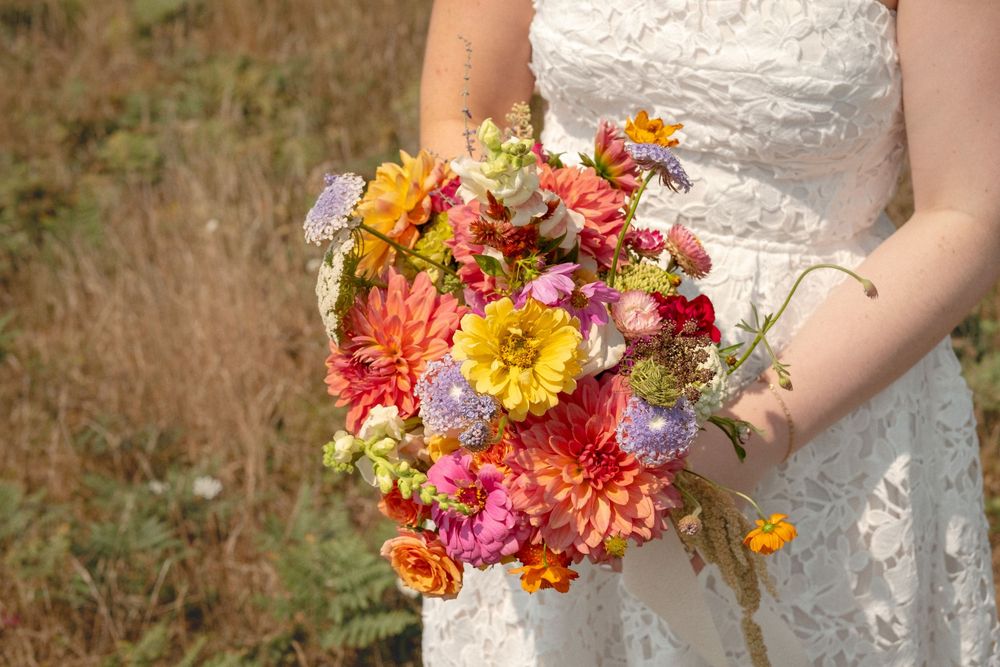 A close-up of a bridal bouquet featuring coral and yellow dahlias with lace dress details.