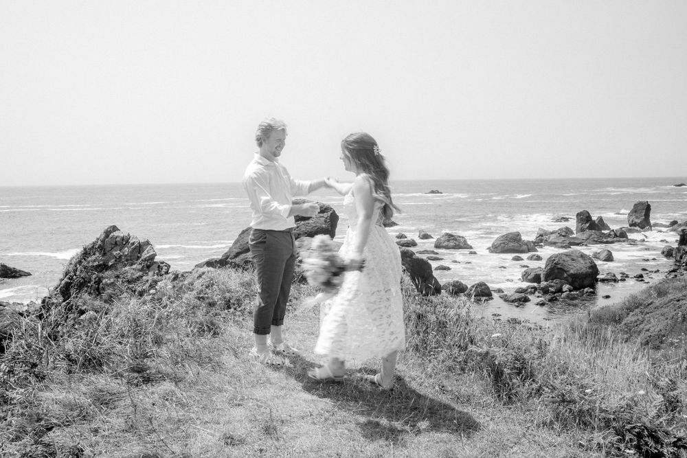 A couple shares a romantic moment on a coastal cliff overlooking the ocean and rock formations.
