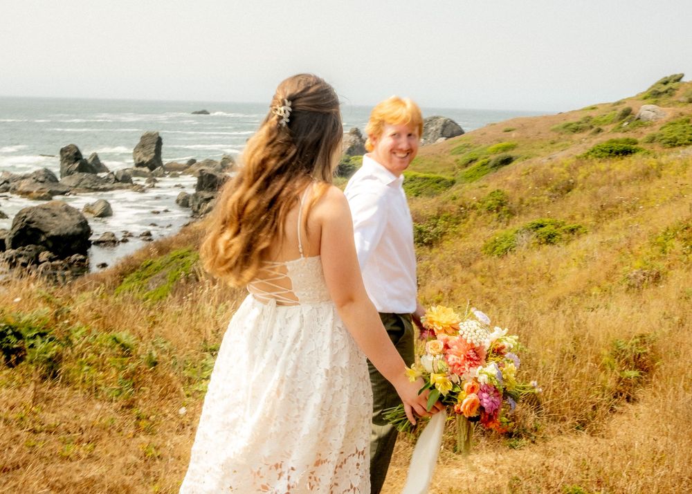 A couple poses on a scenic coastal hillside with vibrant wildflowers and ocean views.