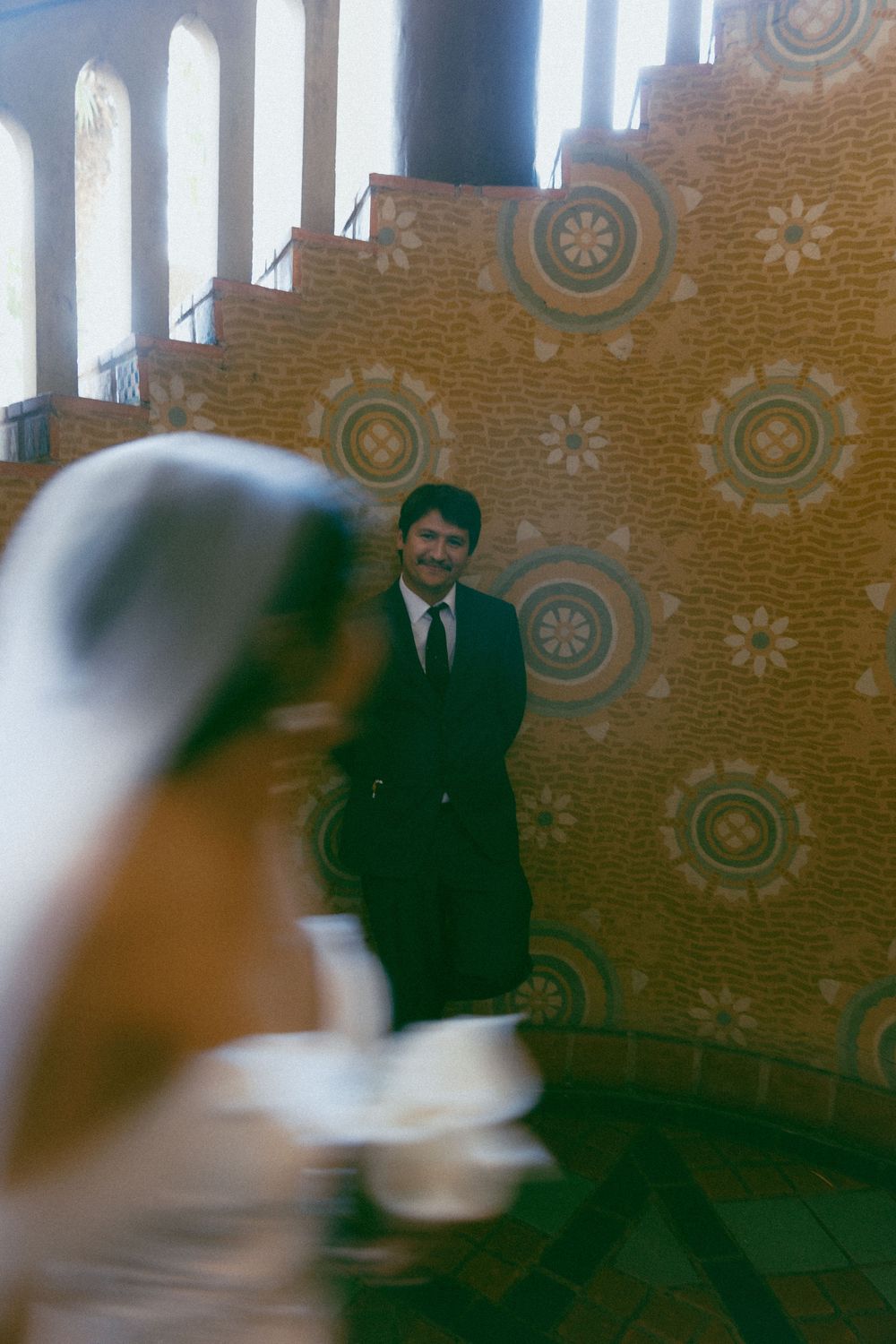 A blurred vintage photograph shows people in dark business suits standing against a decorative patterned wall.