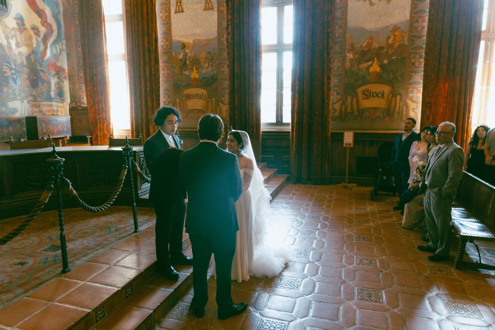 A couple celebrates their intimate wedding ceremony inside a historic castle room with ornate murals and tiled floors.