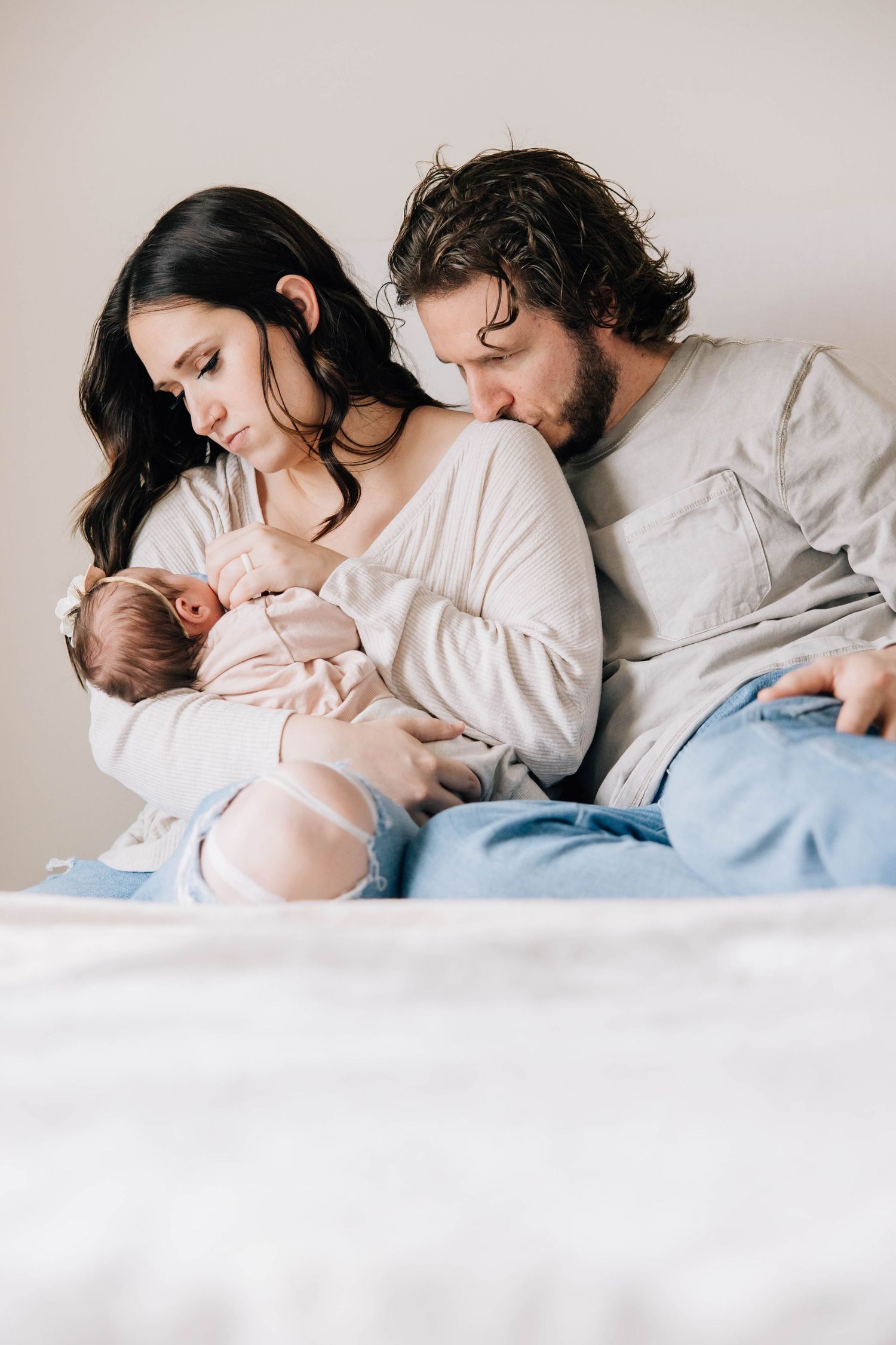 New parents tenderly gazing at their newborn baby while sitting on a bed.