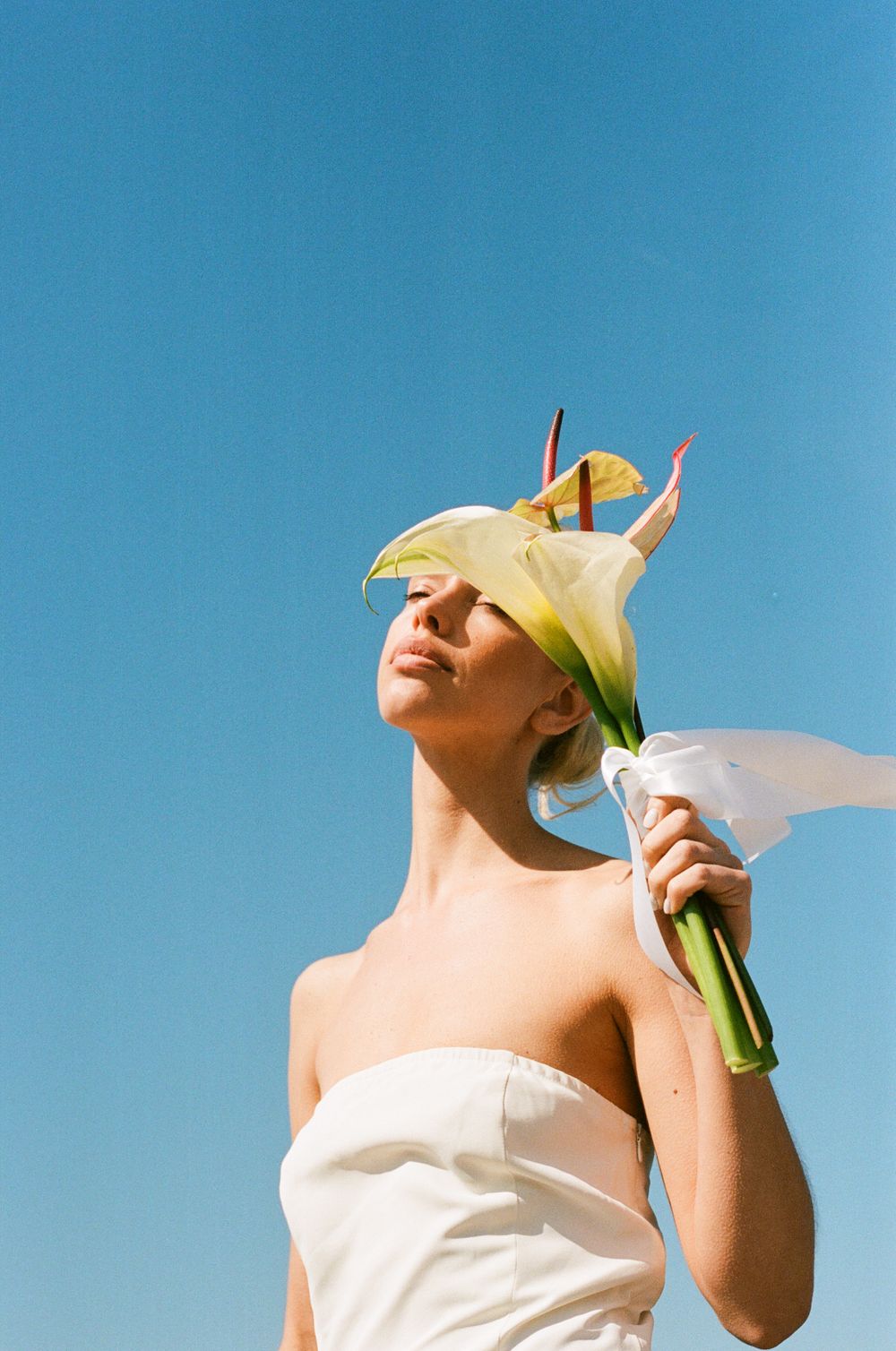 A minimalist editorial Paris portrait against blue sky with a white calla lily flower held up in a white dress.
