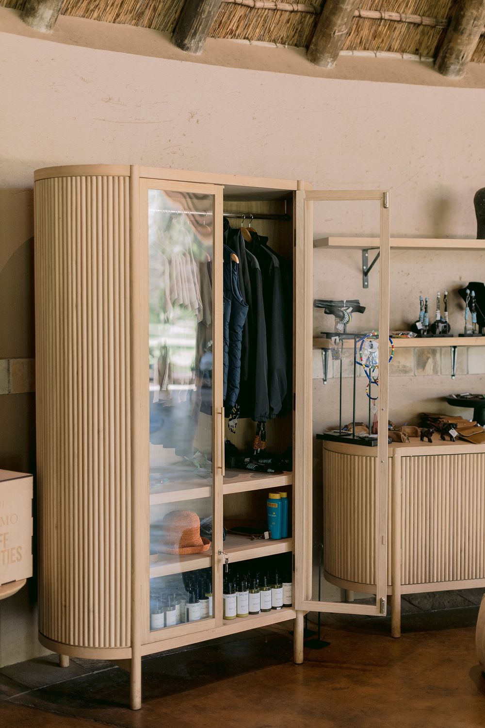 Modern light wood wardrobe with glass doors displaying hanging clothes and shelved items in a lodge room.