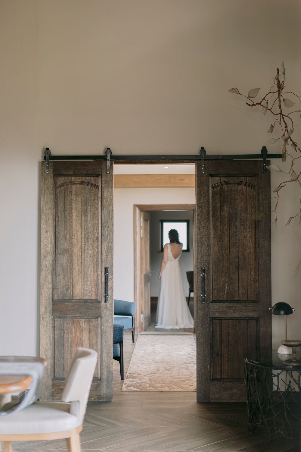 Bride in white wedding gown visible through rustic wooden barn doors in a luxury lodge suite.