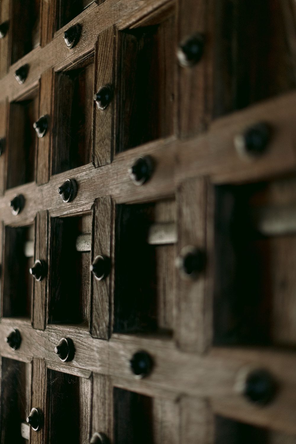 Close-up of an ornate dark wooden door with traditional iron stud detailing and geometric grid pattern.