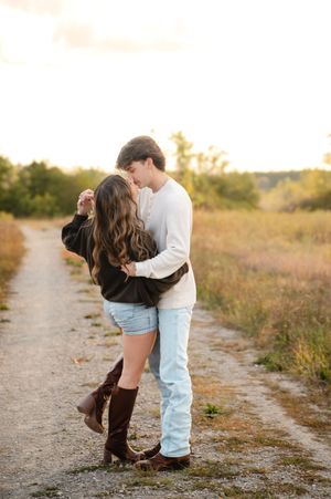 Romantic couple embracing on dirt path during golden hour in countryside setting.