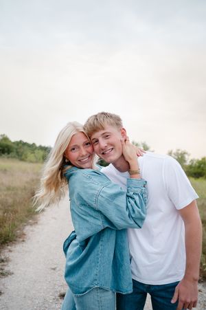 Casual couple in denim and white sharing intimate moment on rural path at sunset.