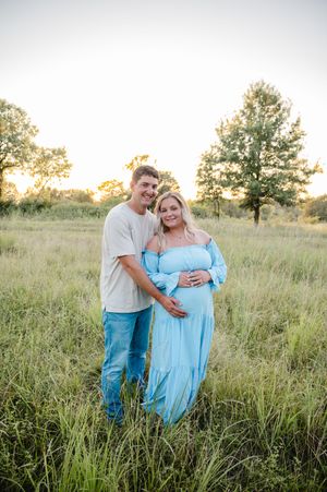Couple embraces in tall grass field during golden hour photoshoot.