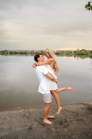 Couple in white outfits plays and dances together on beach at sunset.