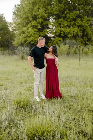 Couple in red dress and black shirt poses together in green summer meadow.