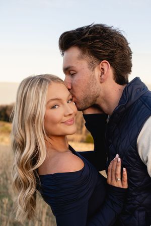 Romantic couple shares tender moment during sunset photoshoot in field.