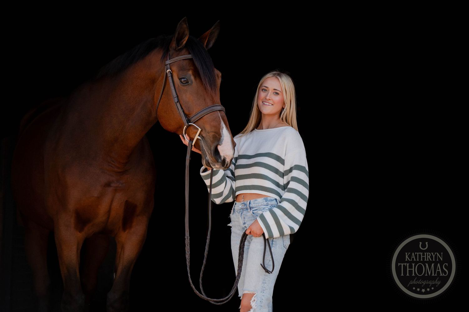 Horse and companion in equestrian portrait against dark background with striped sweater and jeans.