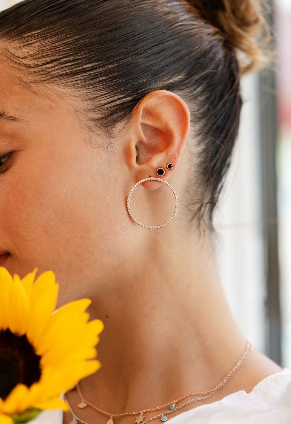 Close-up view of a delicate circular hoop earring with a bright sunflower accent against a soft, natural light background.