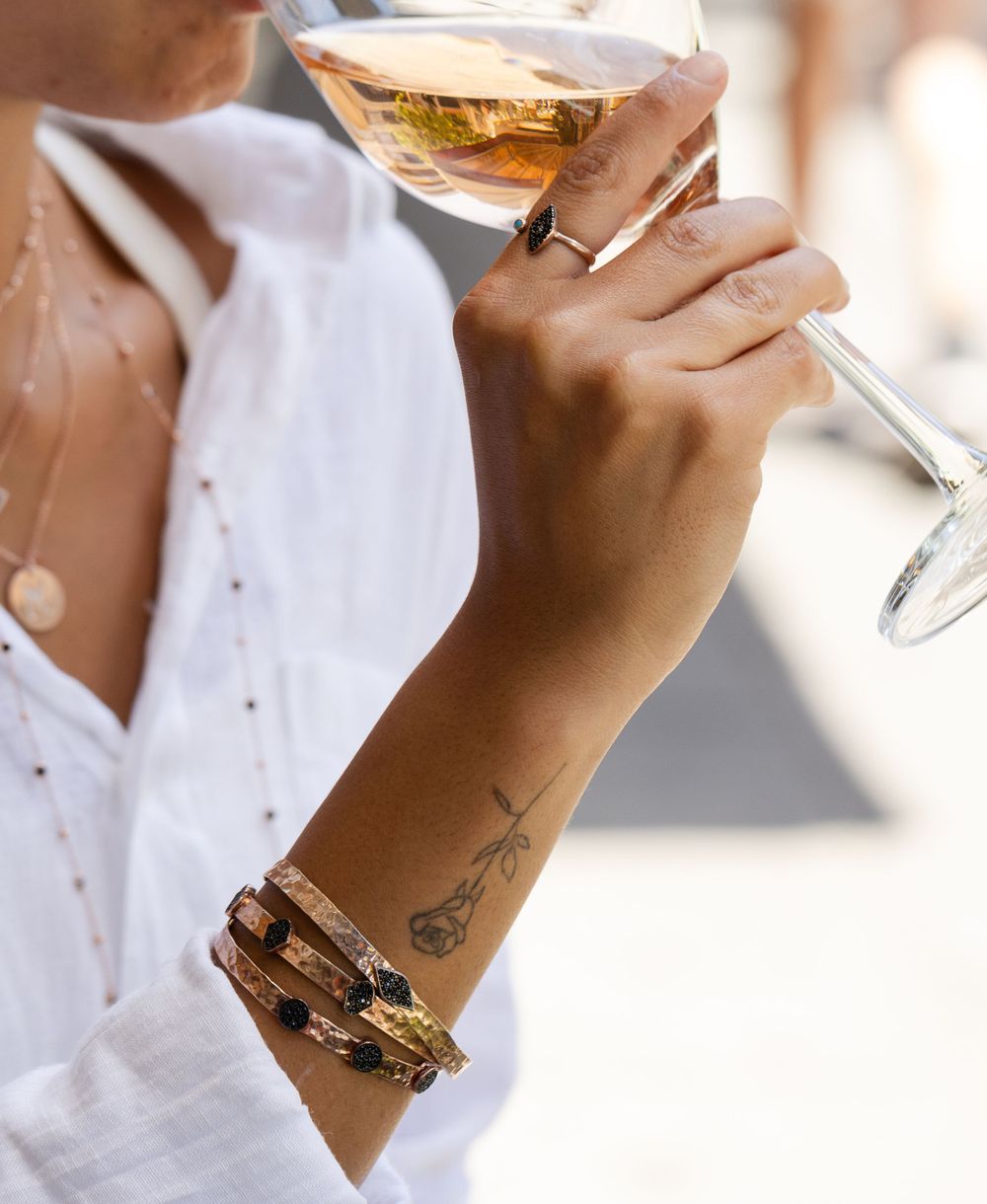 Hand holding wine glass with bracelets and delicate forearm tattoo in elegant setting.