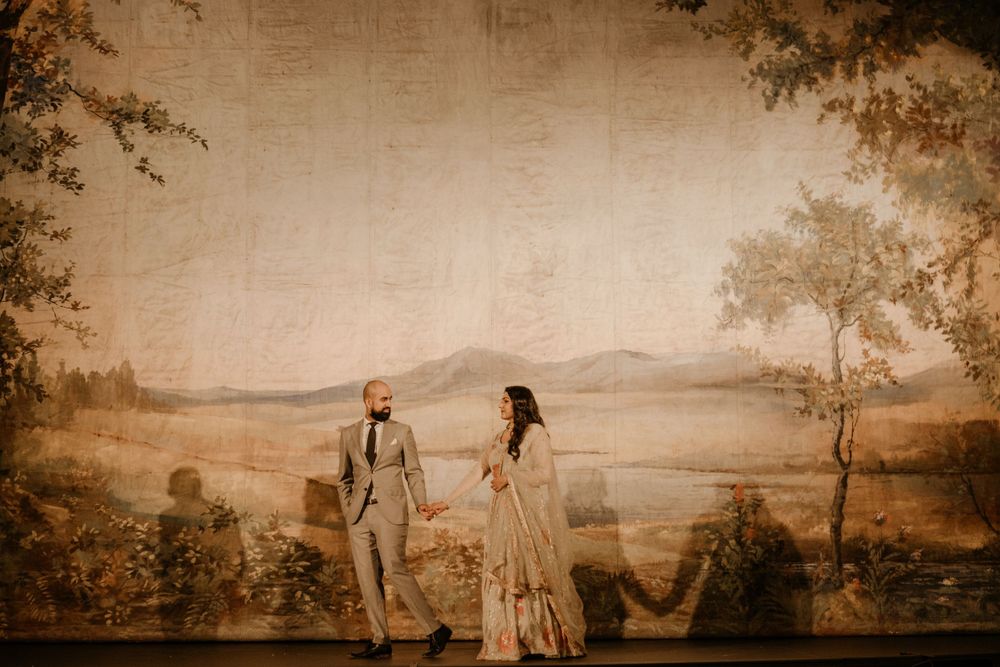 Couple in vintage-inspired wedding attire standing on hill overlooking scenic mountain landscape at golden hour.