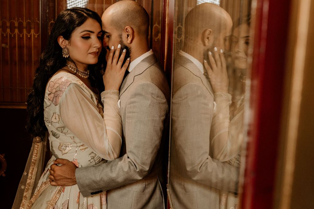 A romantic couple in wedding attire embrace against a rustic wall with reflection, captured in warm moody lighting.