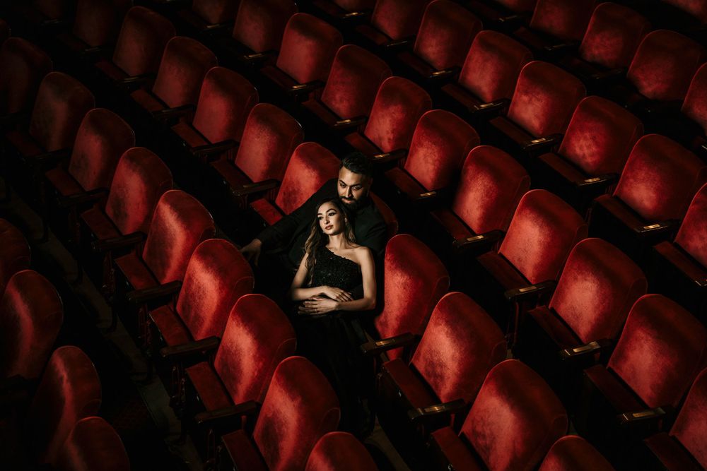 A solitary person sits among rows of empty red theater seats in a darkened auditorium.