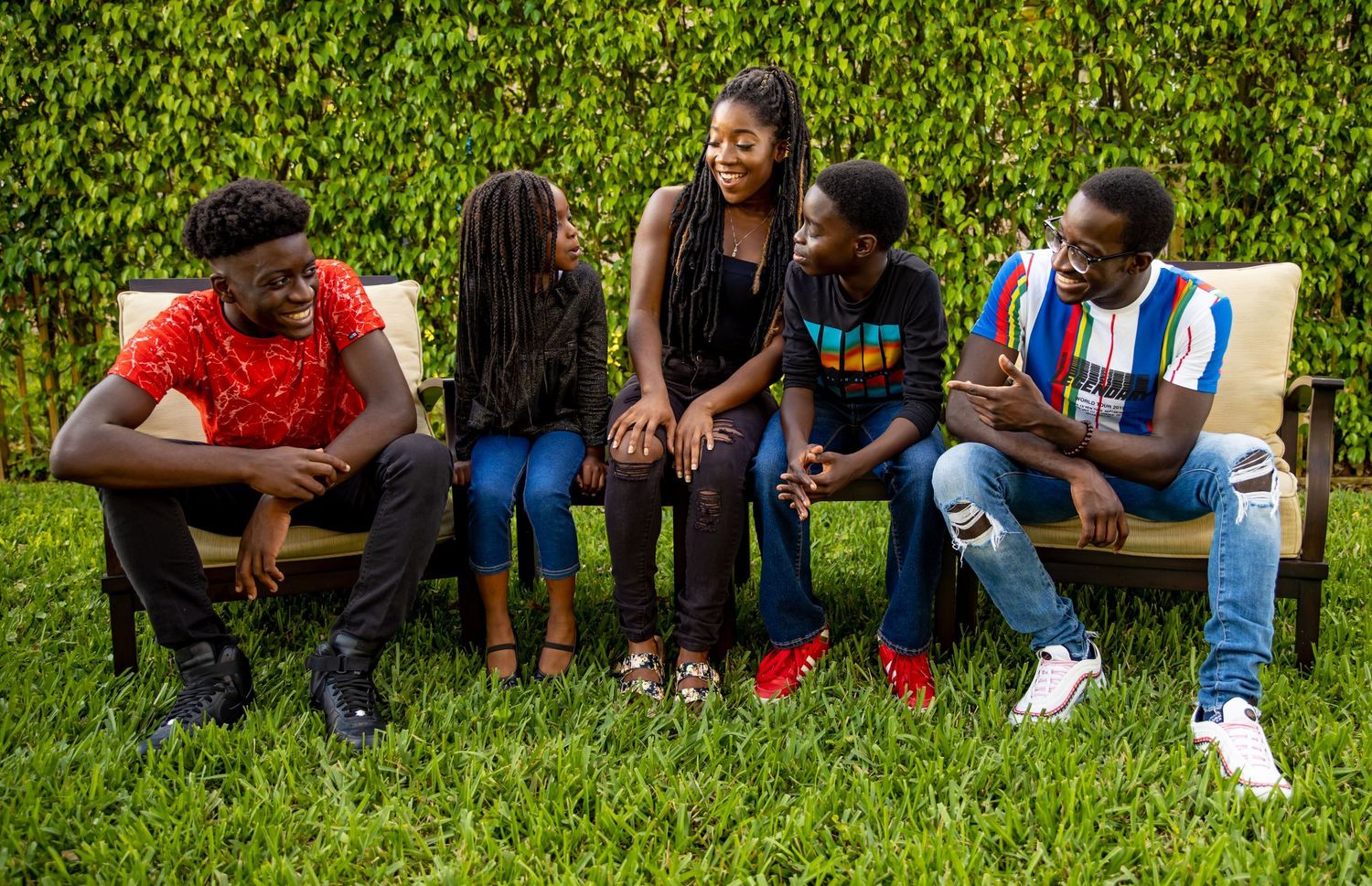 Group of friends sitting casually on a bench against lush green foliage background on a sunny day.