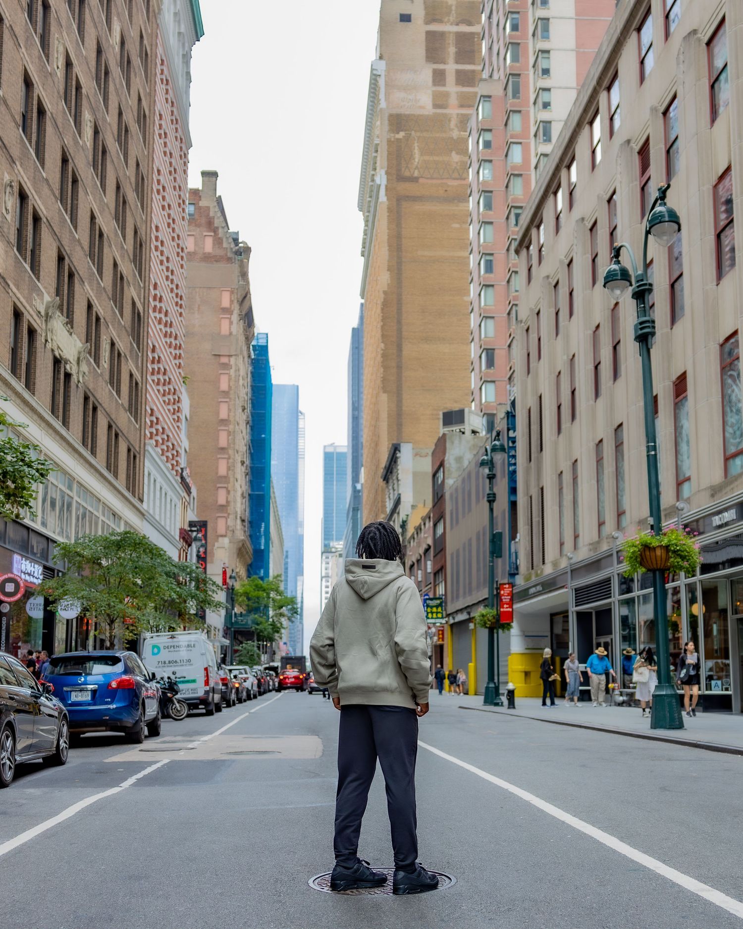 Person in hoodie standing in middle of empty New York City street surrounded by tall buildings.