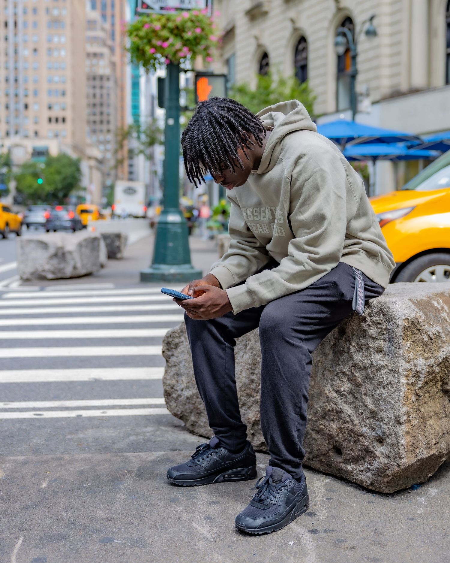 Person in gray sweatshirt checking phone while sitting on stone block in urban setting.