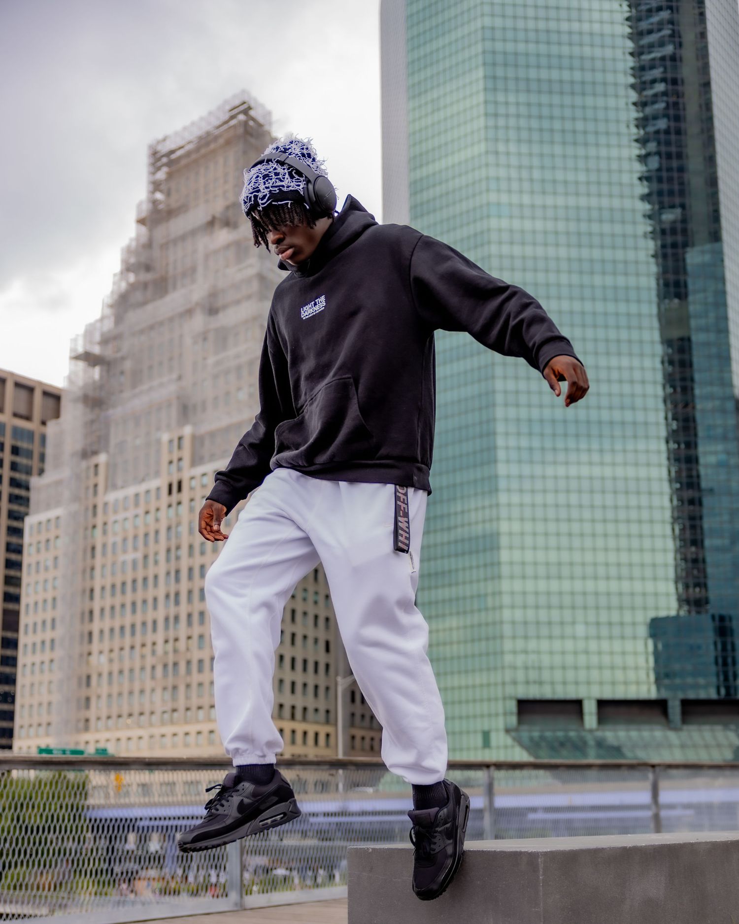 Fashion shot of person jumping on urban platform wearing black hoodie and white pants.