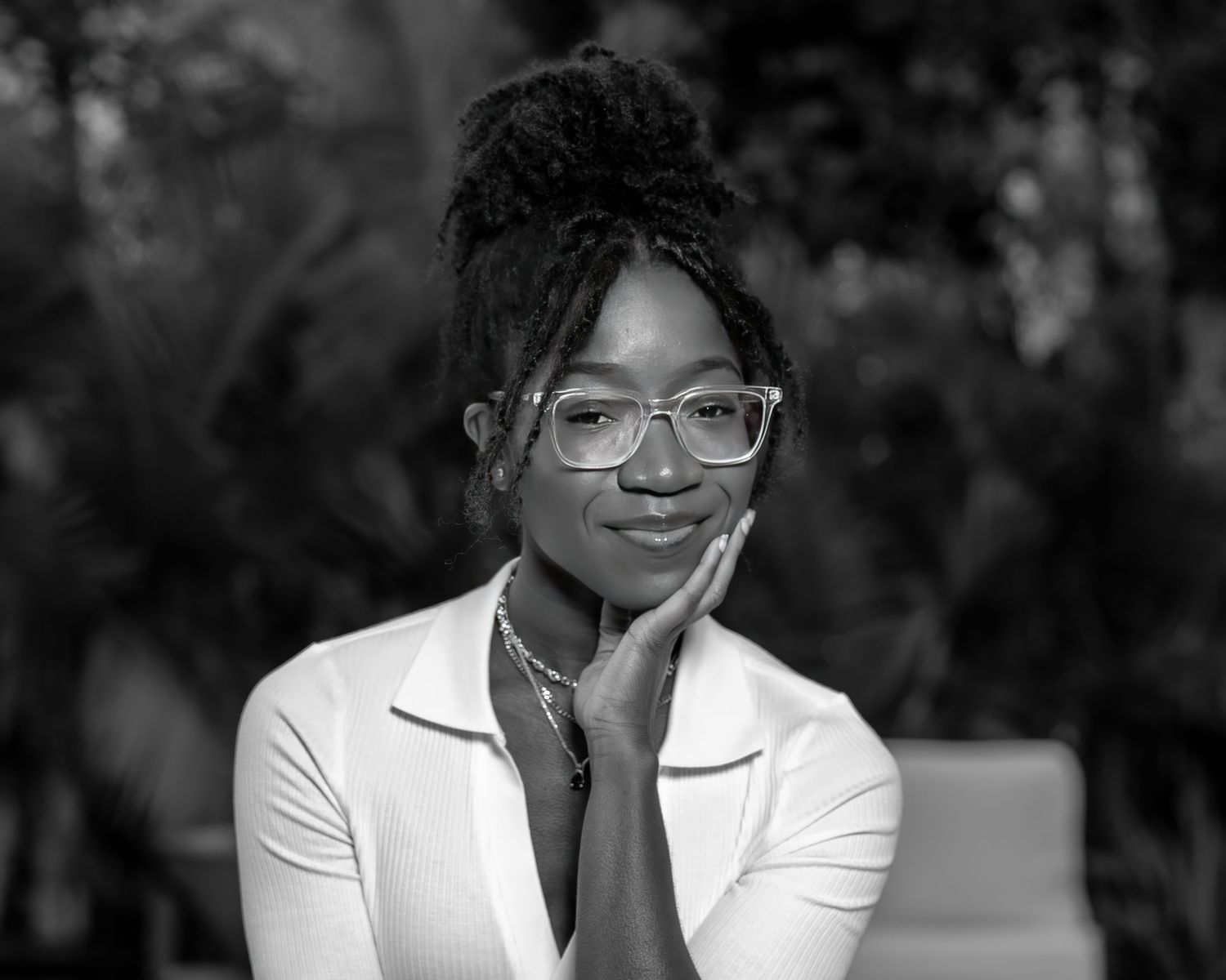 Black and white professional headshot of person in white blazer and glasses.