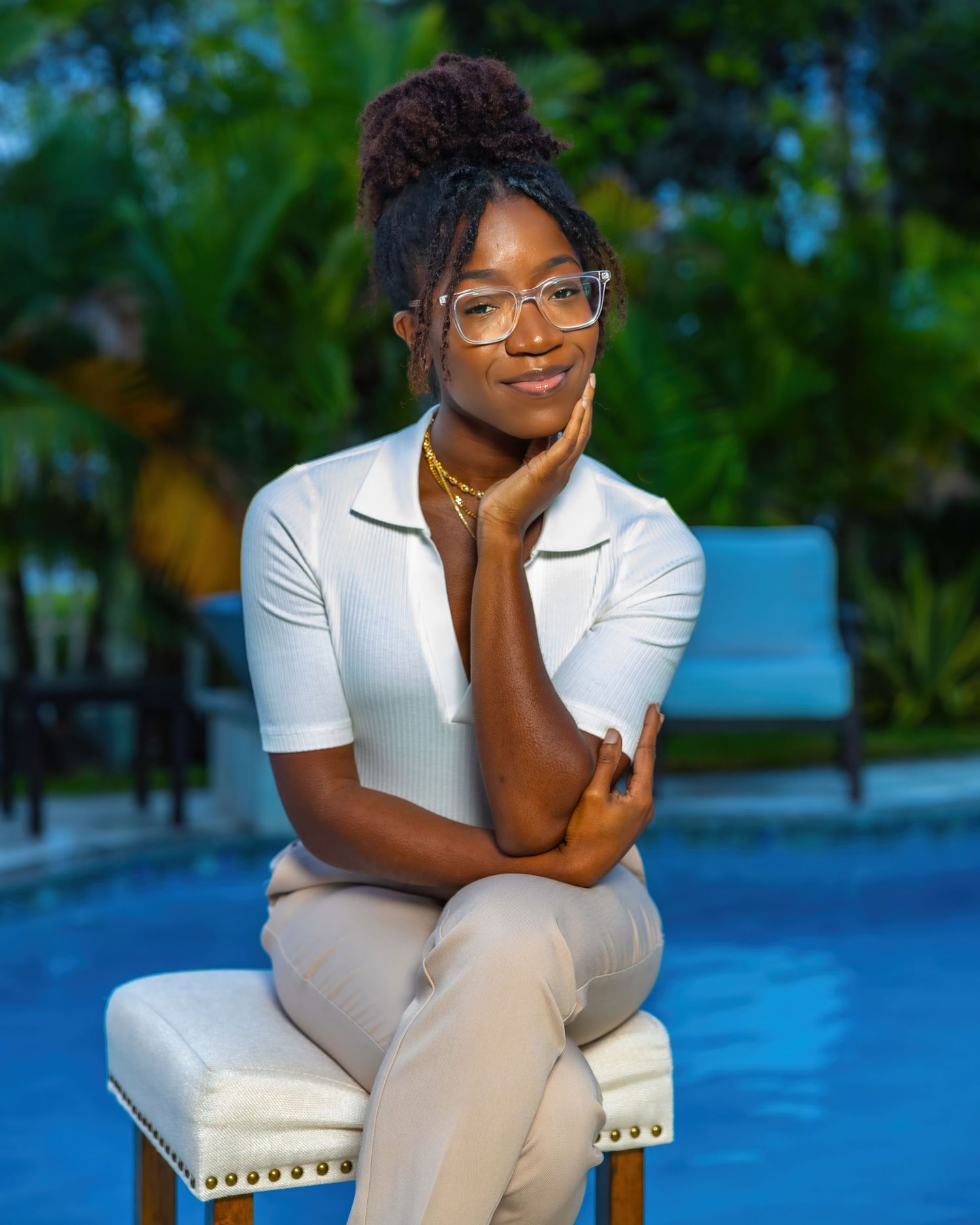 Stylish professional in white top and glasses sits elegantly on a chair against a blue background.