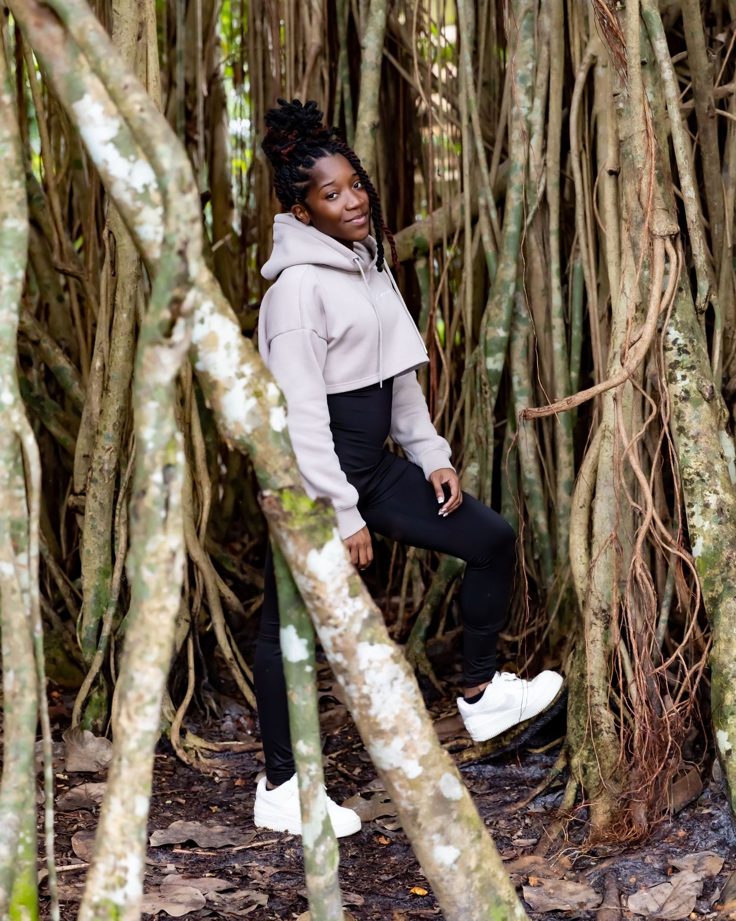 Casual portrait in nature with person posing among twisted tree trunks wearing athletic wear.