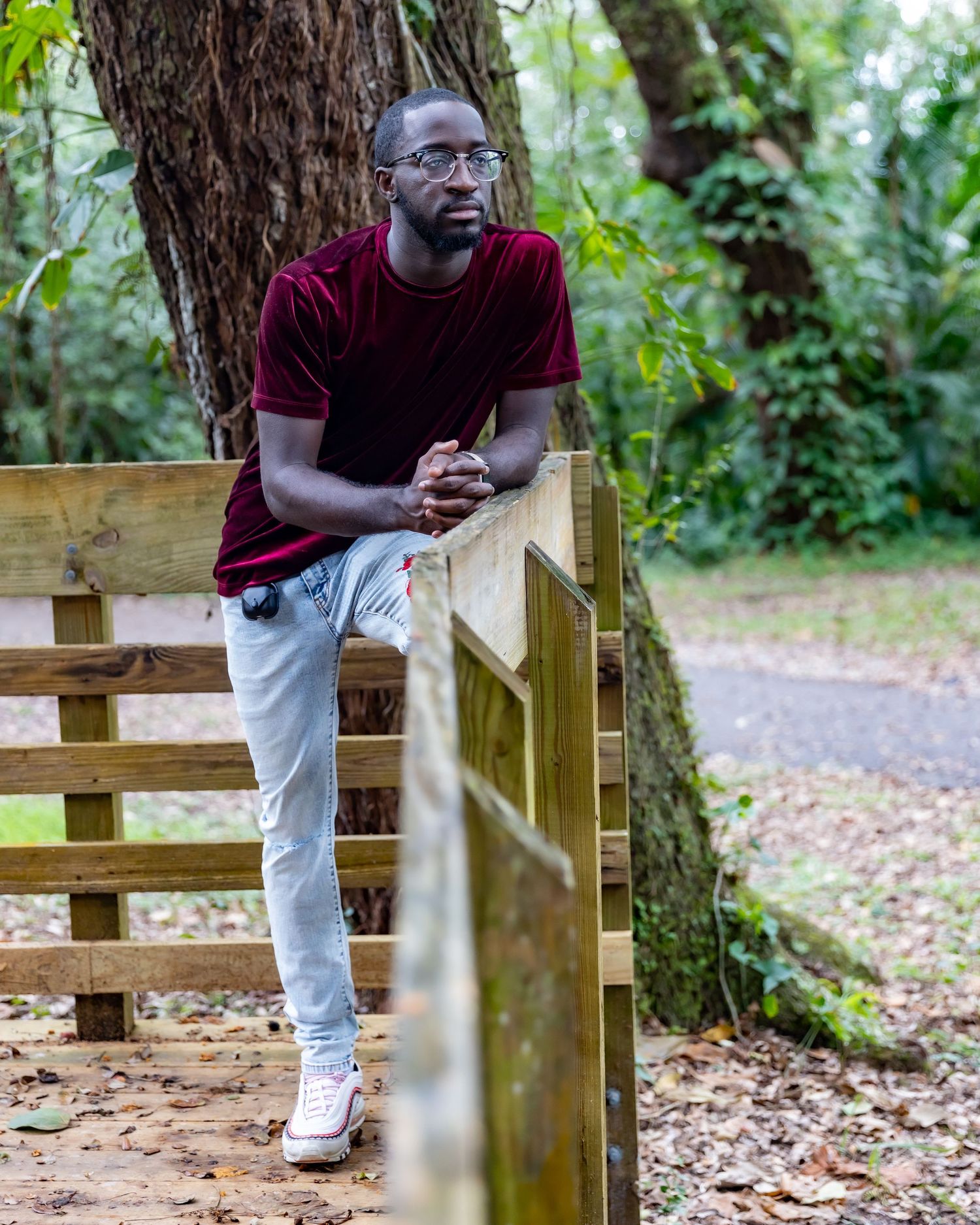 Portrait of person in burgundy velvet shirt leaning on wooden railing in outdoor setting.