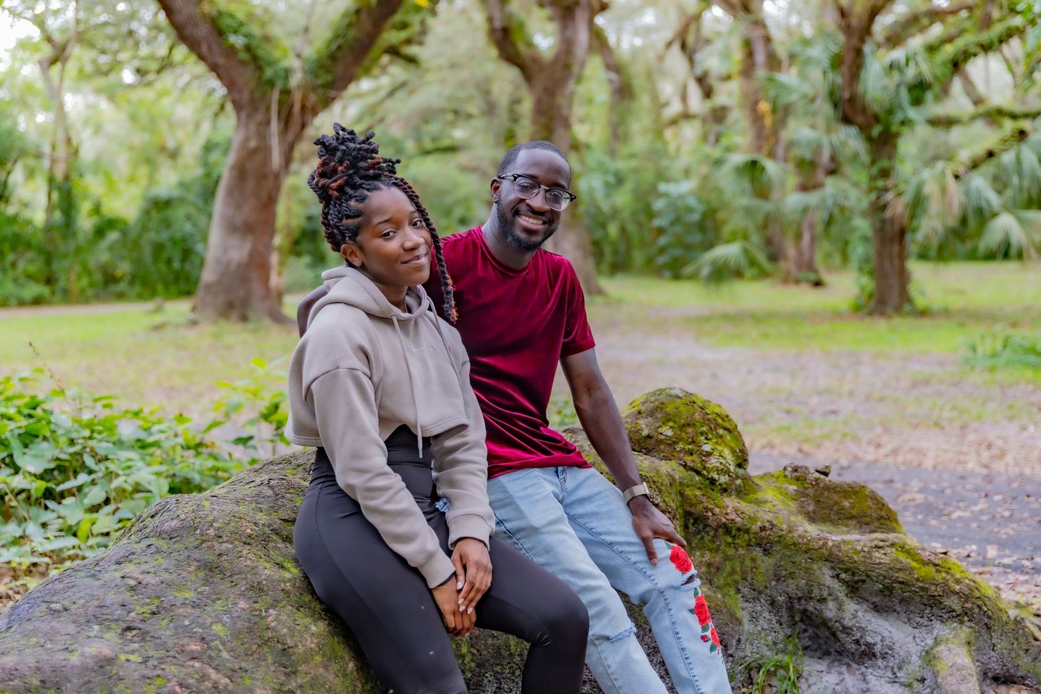 Two people sitting together on mossy rock in wooded outdoor setting.